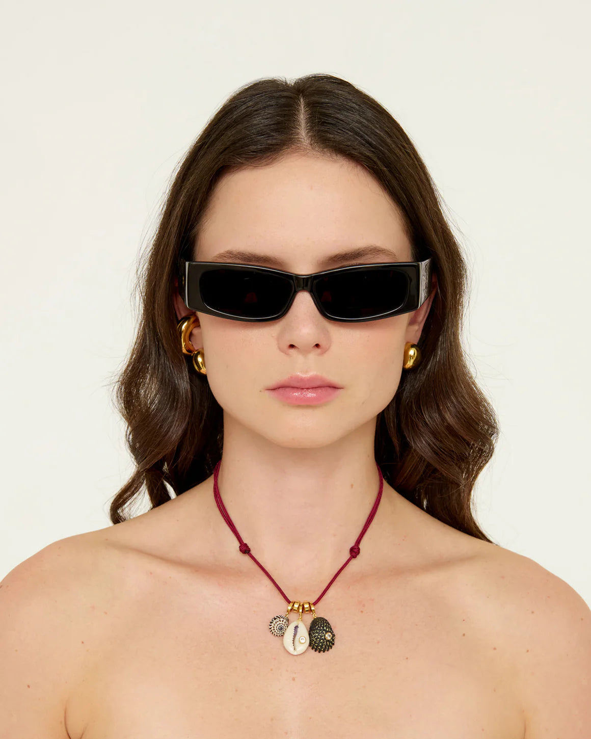 Woman wearing black sunglasses and a red necklace with shell pendants on a white background