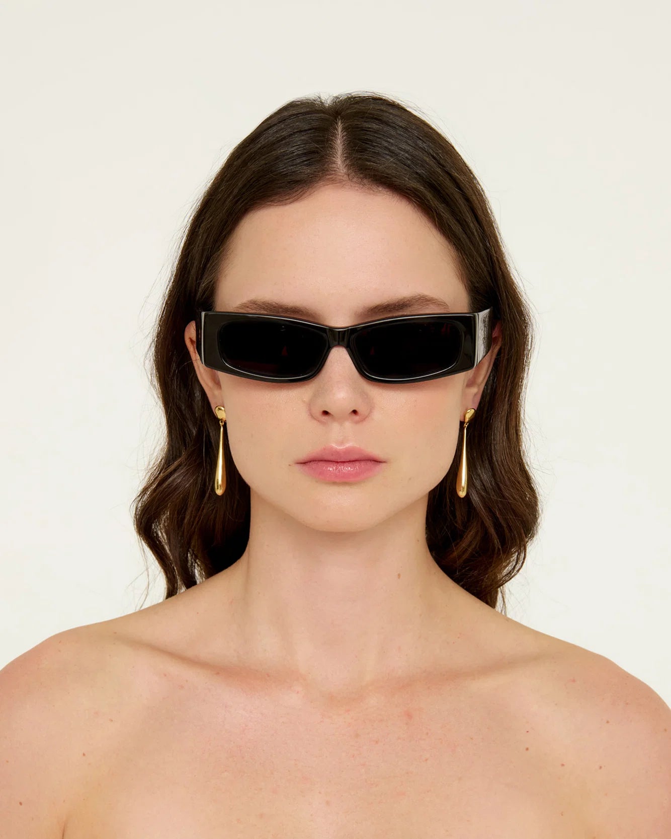 Woman wearing black sunglasses with a gold earring on a plain background
