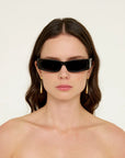 Woman wearing black sunglasses with a gold earring on a plain background