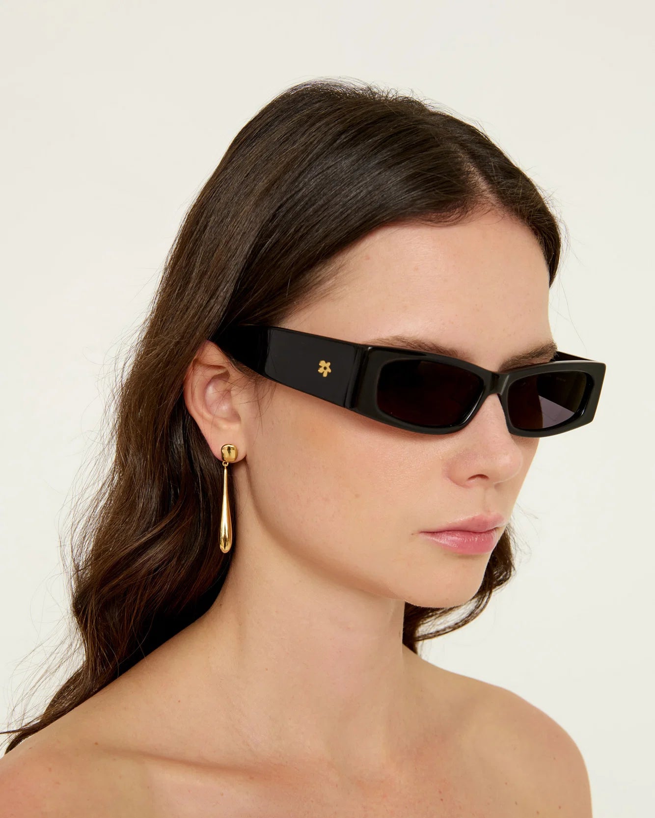 Woman wearing black sunglasses with a gold earring on a plain background