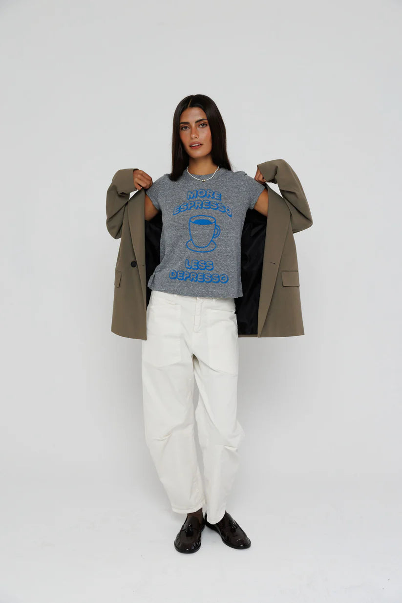 Person wearing a gray t-shirt with text and graphics, white pants, and a brown coat on a white background