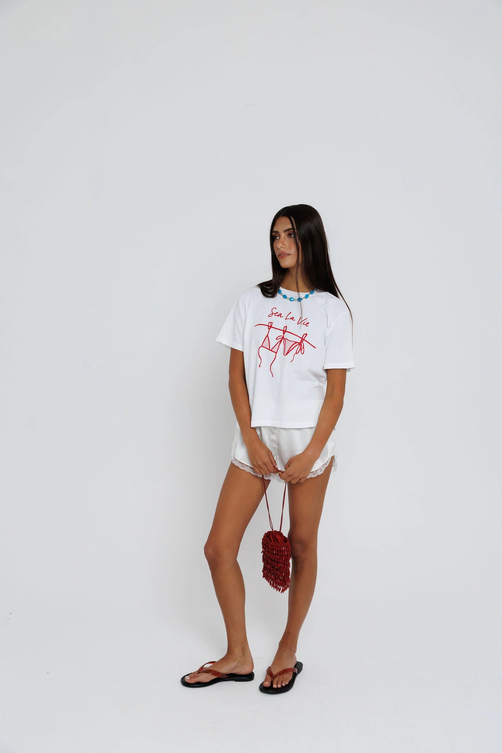 model wearing sea la ie graphic tee with a turquoise necklace on a white background