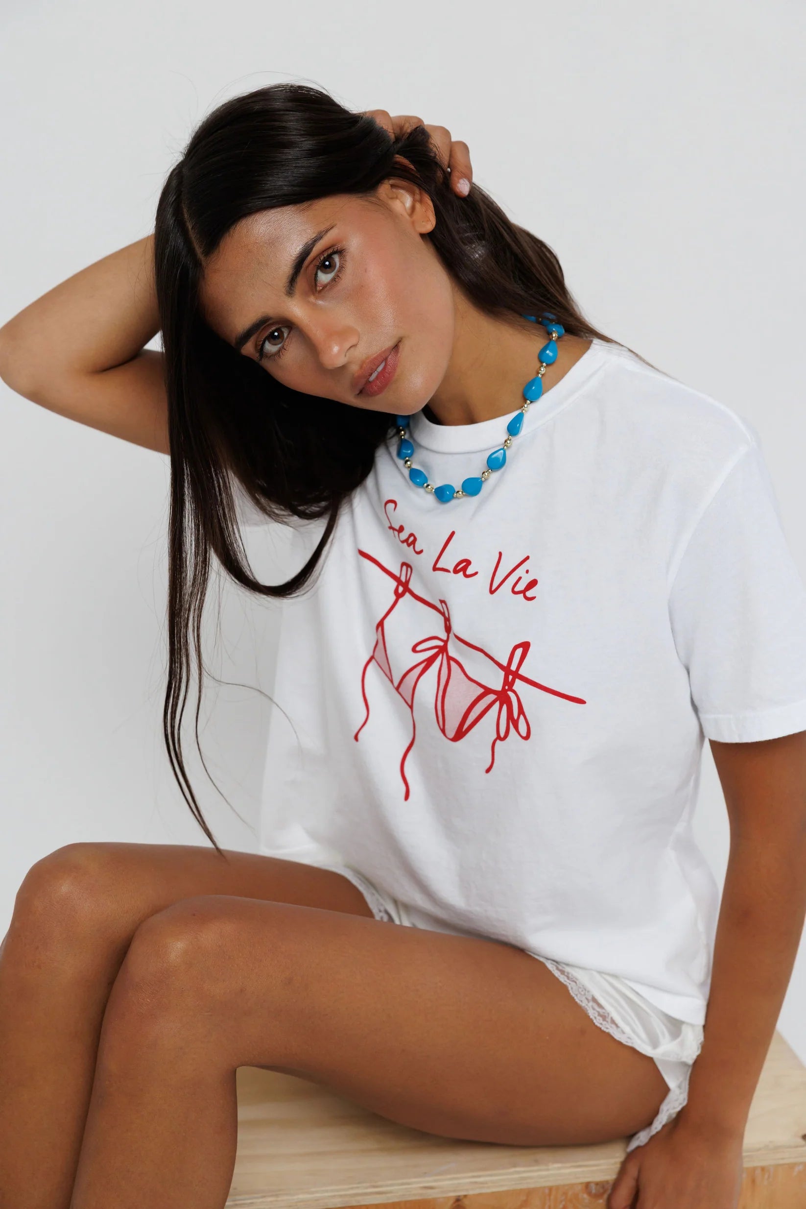 model wearing sea la ie graphic tee with a turquoise necklace on a white background