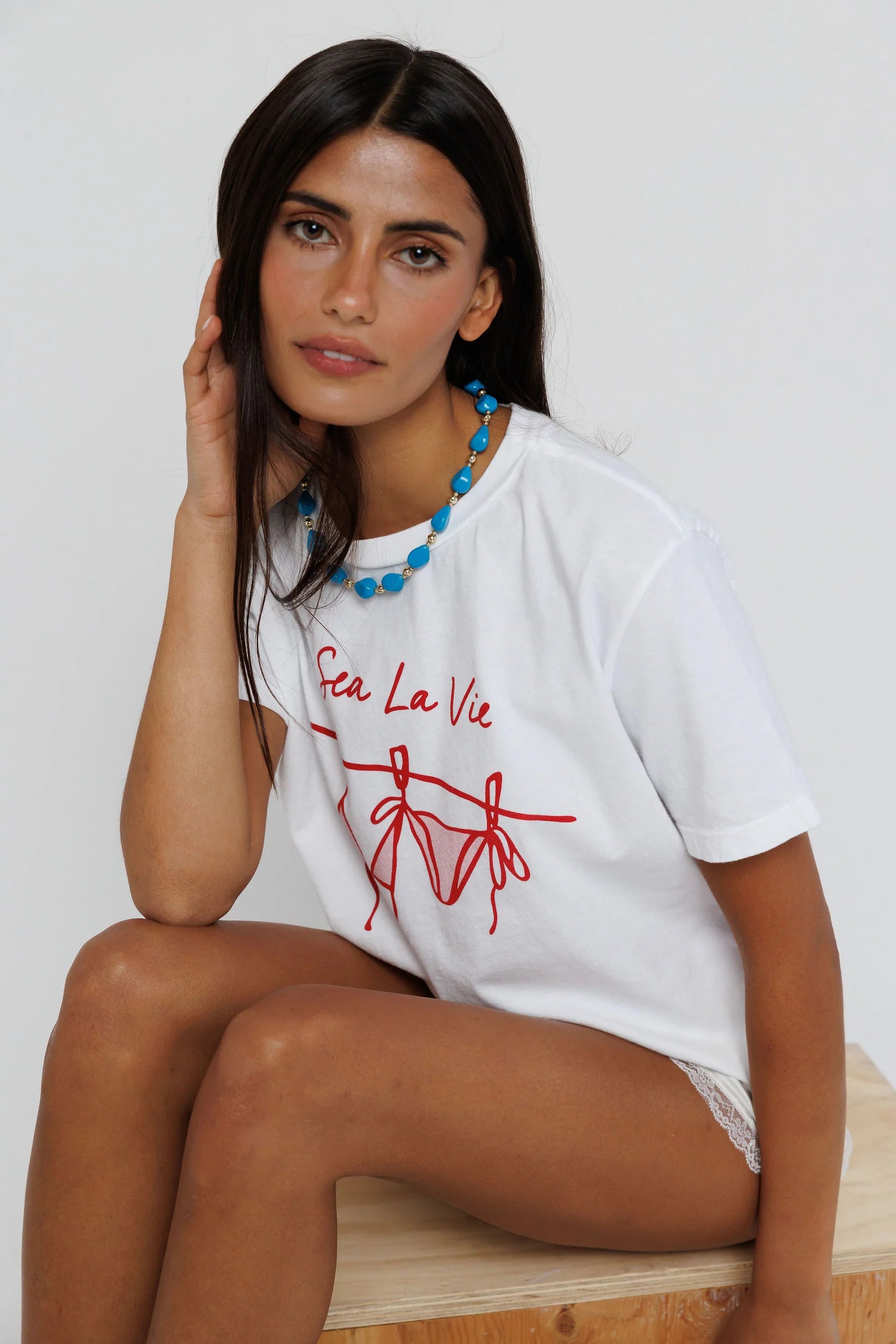 model wearing sea la ie graphic tee with a turquoise necklace on a white background