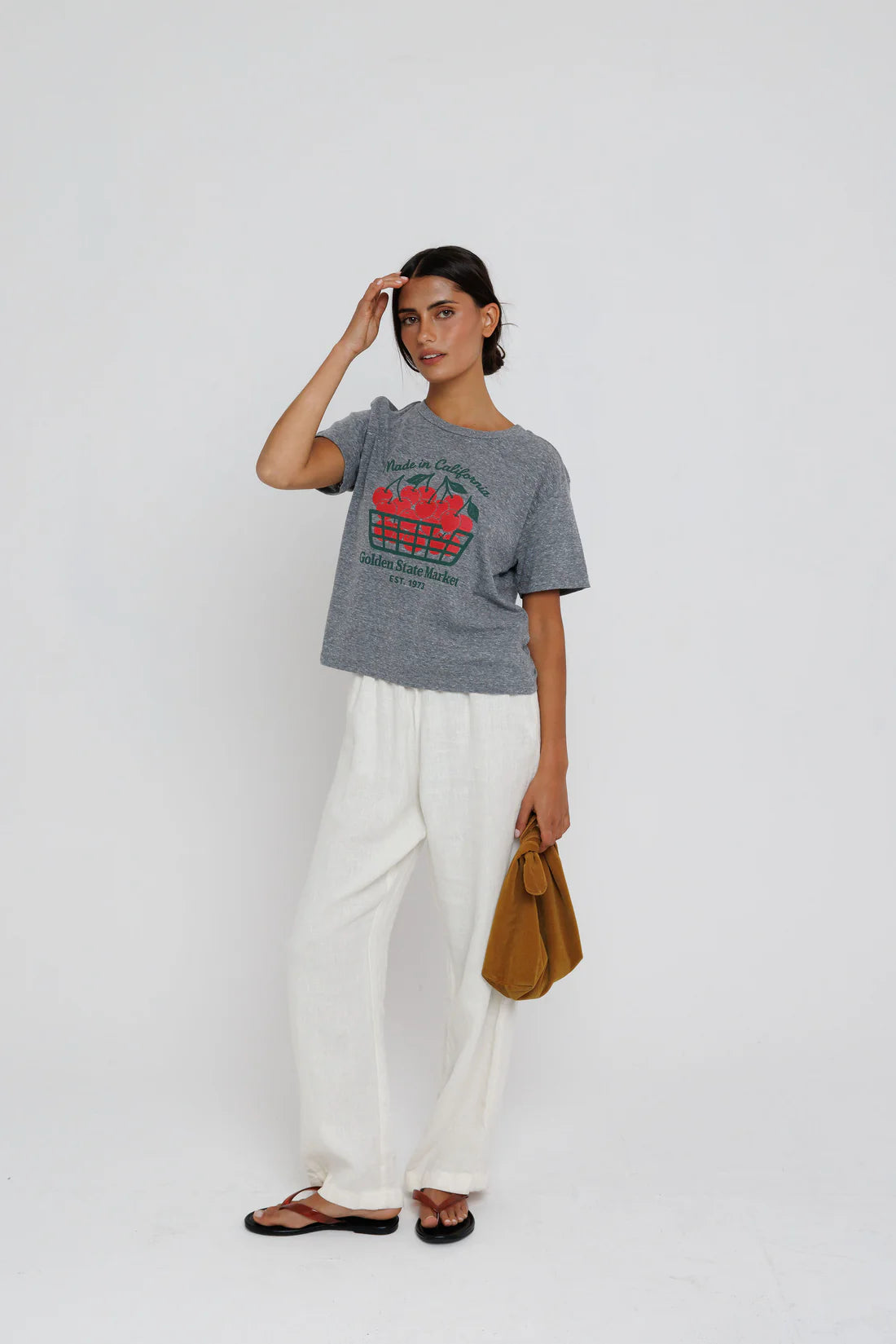 Woman wearing a gray t-shirt with a graphic design and white pants, standing against a plain background.