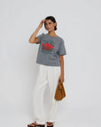 Woman wearing a gray t-shirt with a graphic design and white pants, standing against a plain background.