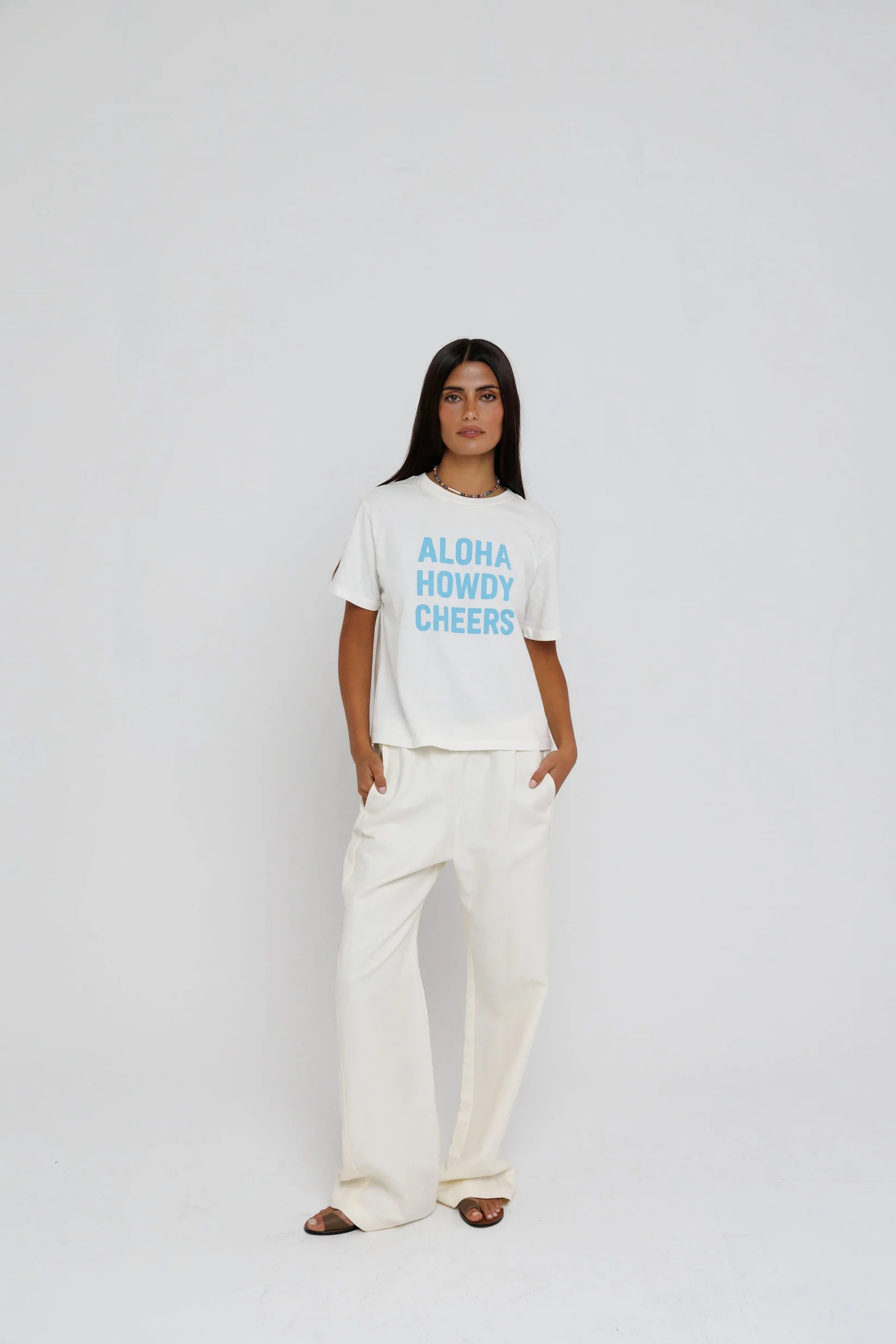 model wearing aloha howdy cheers short sleeve tee with white pants on a white background