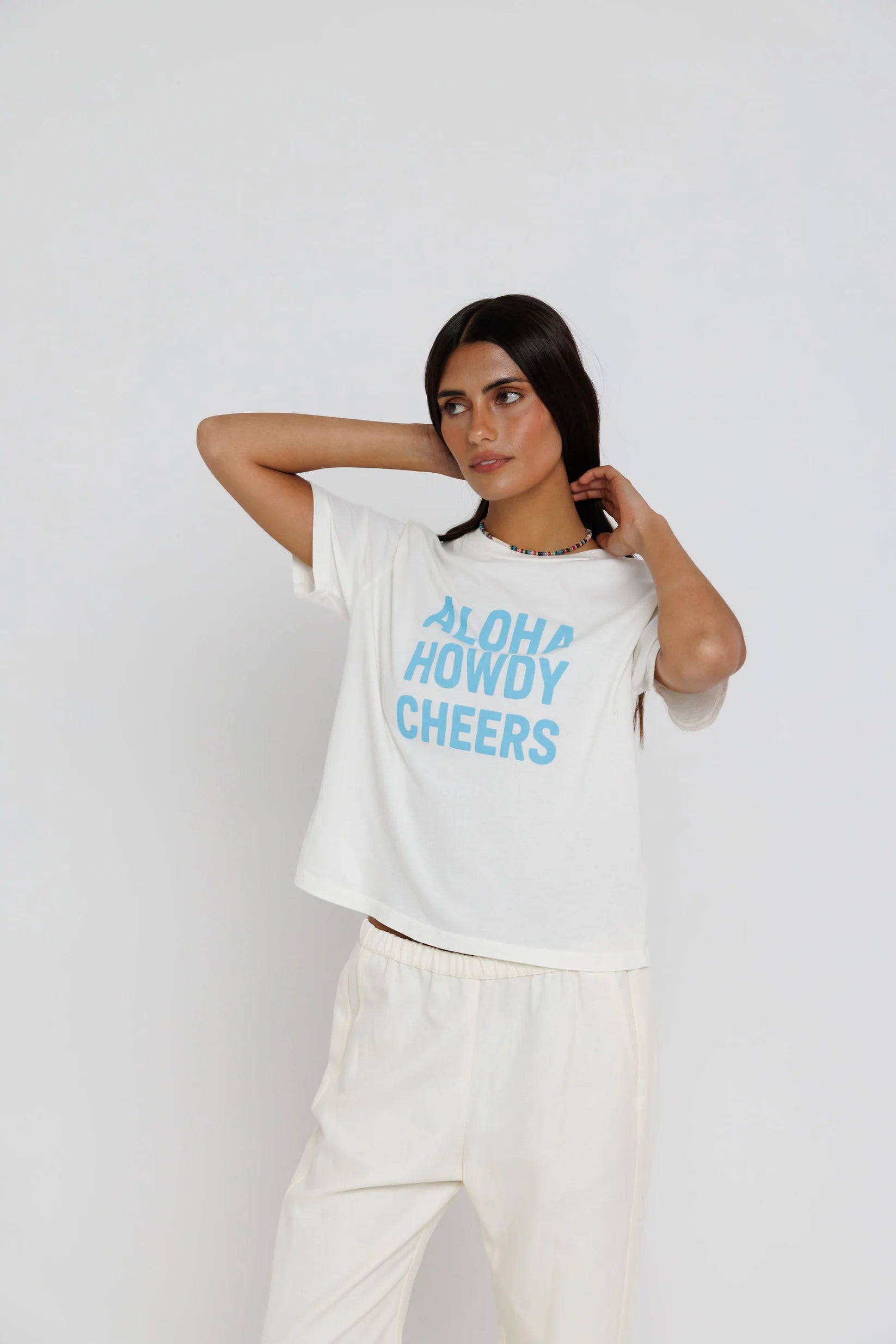 model wearing aloha howdy cheers short sleeve tee with white pants on a white background