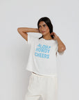 model wearing aloha howdy cheers short sleeve tee with white pants on a white background