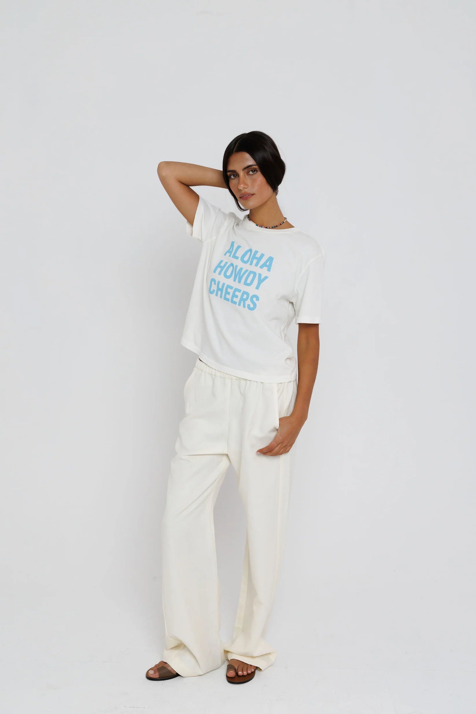 model wearing aloha howdy cheers short sleeve tee with white pants on a white background