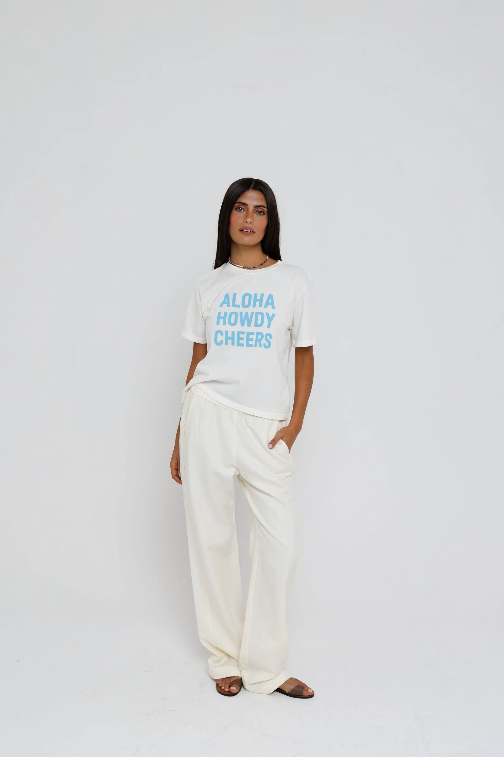model wearing aloha howdy cheers short sleeve tee with white pants on a white background