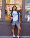 Woman wearing a 'Book lub t-shirt and sweater standing in front of a store window.