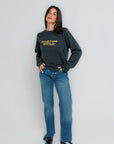 Woman wearing a dark gray sweatshirt with yellow text and blue jeans on a white background