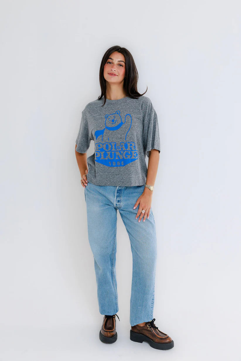 Person wearing a gray t-shirt with blue graphic and text, paired with light blue jeans on a white background, full body
