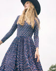 Woman wearing a patterned dress and black hat against a blurred natural background