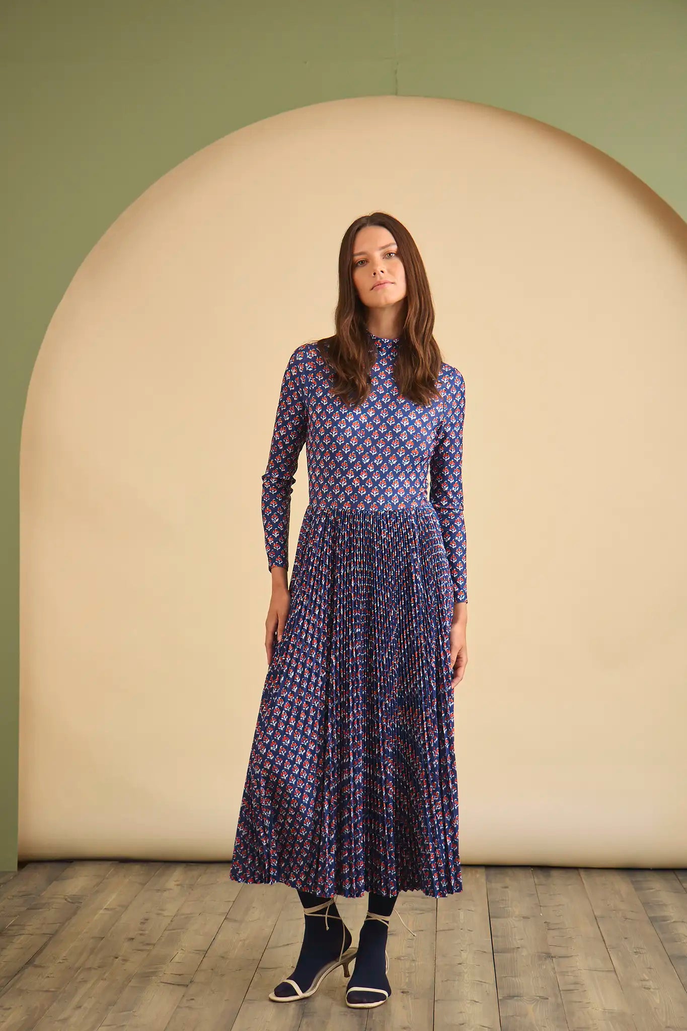 Woman wearing a blue patterned dress standing in front of a beige archway.