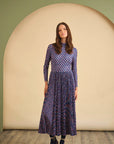 Woman wearing a blue patterned dress standing in front of a beige archway.