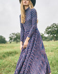 Woman in a patterned dress and wide-brimmed hat standing in a field.