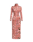 A long-sleeve, high-neck maxi dress with a pink base and an intricate multicolor patchwork-style floral and geometric pattern, shown on a plain white background.