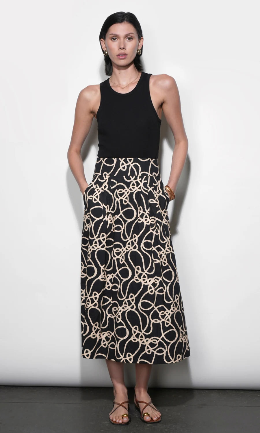 Woman wearing a black sleeveless top and a long, patterned skirt on a white background