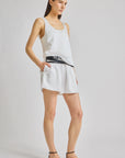Woman wearing a white sleeveless top and shorts with a black belt on a light gray background