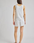 A woman shown from the back wearing a sleeveless white top and matching white shorts against a light gray studio background.