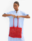 Woman holding a red woven handbag against a white background