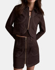 model wearing a chocolate jacket with matching mini skirt with gold zipper on a white background