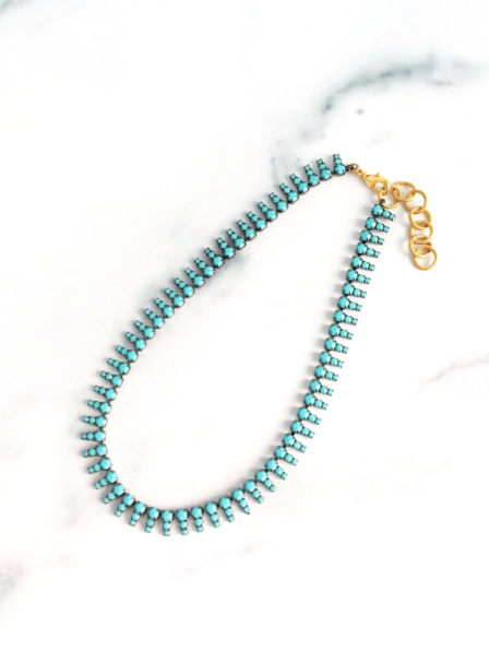 Turquoise beaded necklace with a gold clasp on a white marble surface