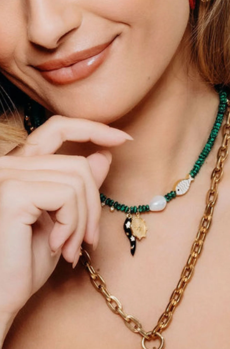Close-up of a woman wearing a gold chain necklace with green beaded necklace.