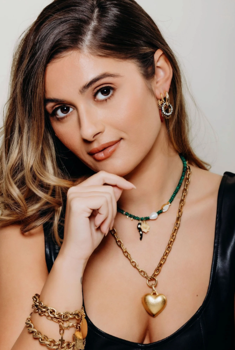 Woman wearing gold necklaces and earrings with a neutral background