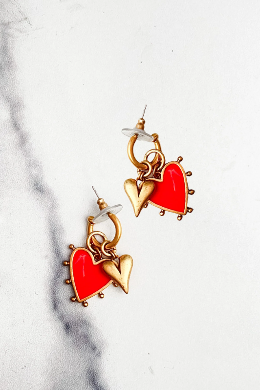 Heart-shaped earrings with gold and red details on a marble surface