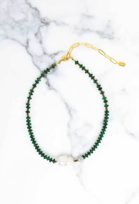 Green beaded necklace with a pearl on a marble surface