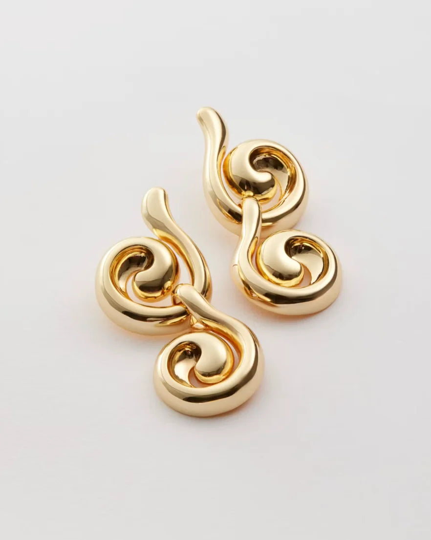 A pair of gold-toned, sculptural spiral earrings with a polished metallic finish, displayed on a clean light gray background.