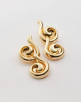 A pair of gold-toned, sculptural spiral earrings with a polished metallic finish, displayed on a clean light gray background.