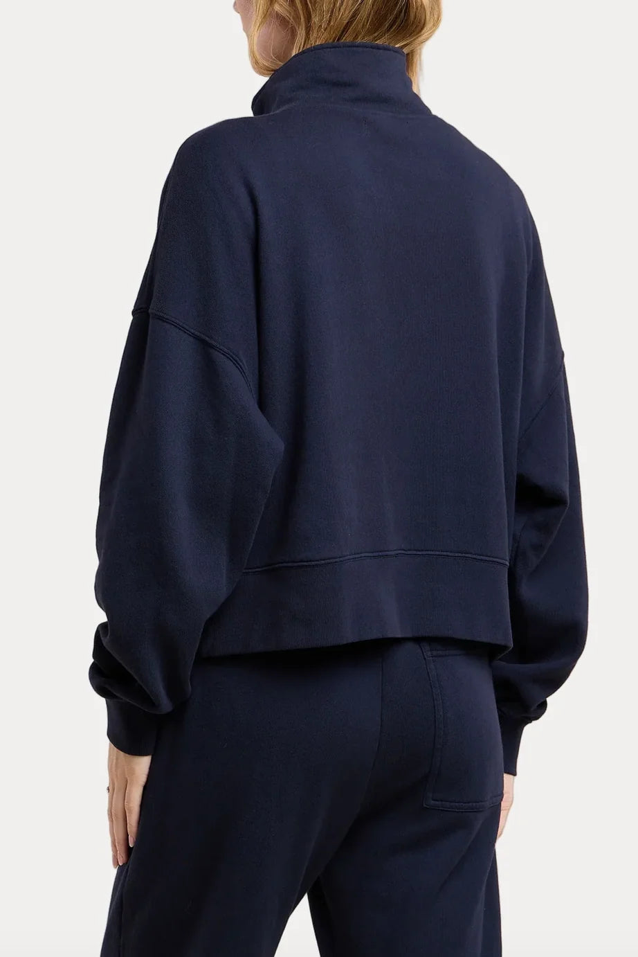A person shown from the back wearing a dark navy cropped sweatshirt and matching navy pants against a clean light gray studio background.