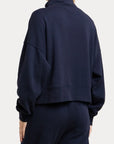 A person shown from the back wearing a dark navy cropped sweatshirt and matching navy pants against a clean light gray studio background.