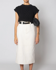 A model stands against a light gray studio background wearing a black short-sleeve textured knit top, a white midi skirt with a black belt, black sunglasses, black strappy heels, and a black woven crossbody bag.