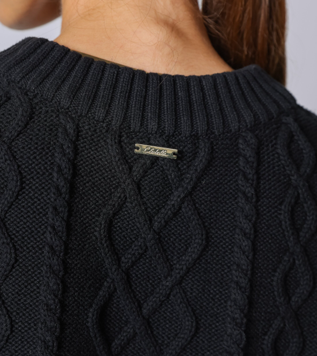 Close-up back view of a person wearing a black cable-knit sweater, showing the neck and upper back with a small metal brand tag reading 'CLEOBELLA' at the center.