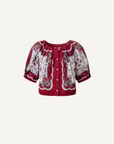 A short-sleeve button-front blouse with a deep V-neck, featuring a red base with a white floral and paisley pattern, displayed on a light cream background.