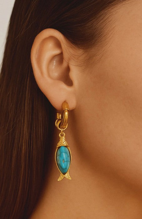 Gold earring with turquoise stone fish charm worn by a person