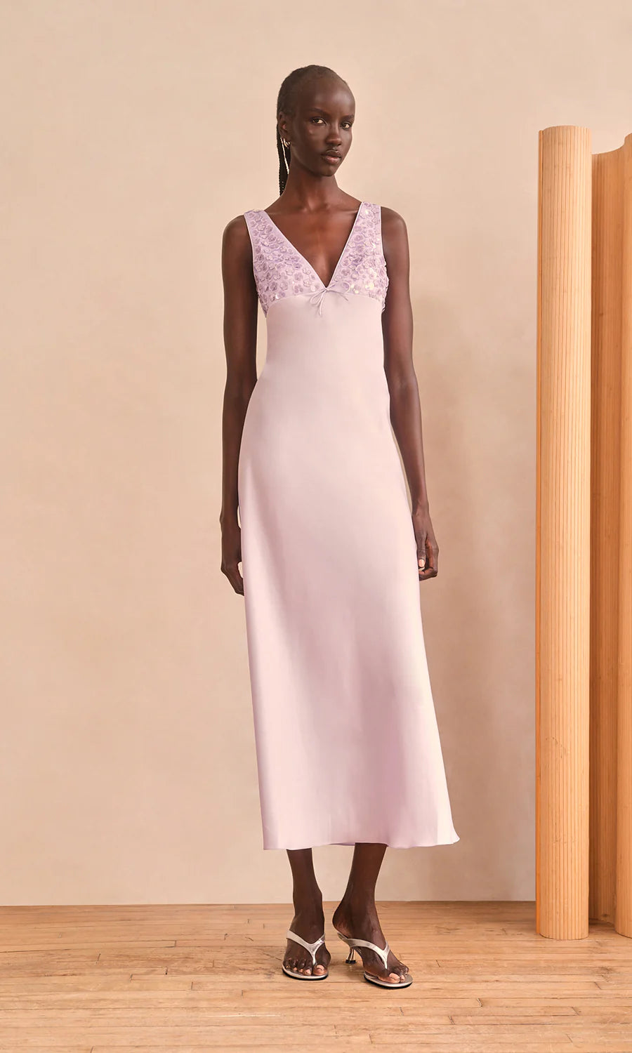 Woman wearing a light purple dress with sequin detailing in a minimalistic setting.