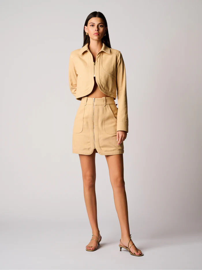 Woman wearing a beige outfit with a jacket and shorts on a plain background