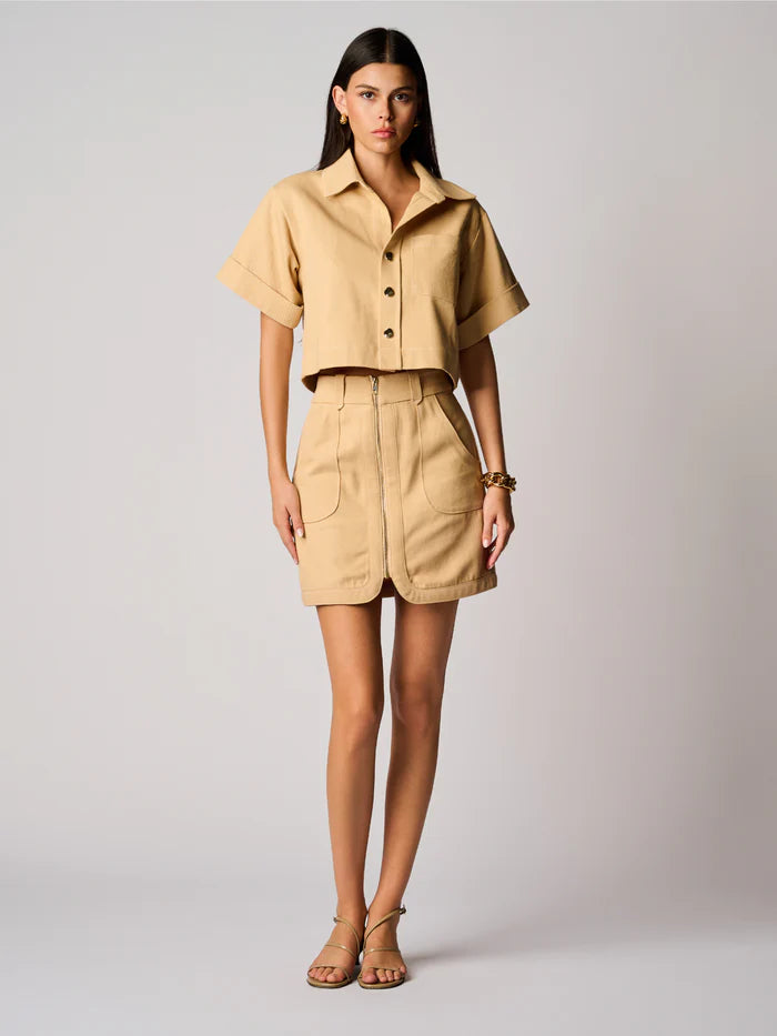 Woman wearing a beige outfit with a shirt and skirt on a plain background