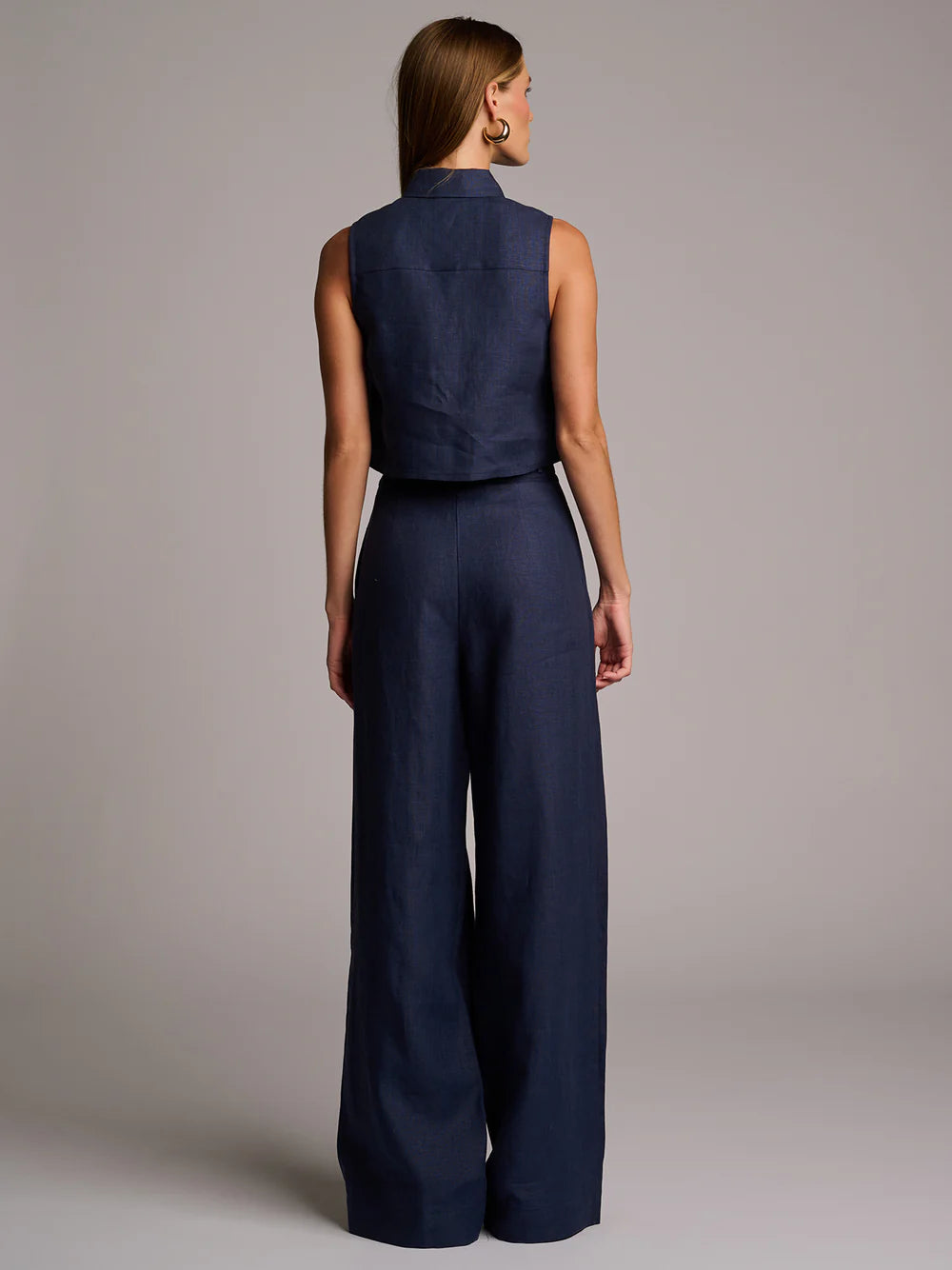 Woman wearing a navy blue sleeveless top and wide-leg pants against a gray background
