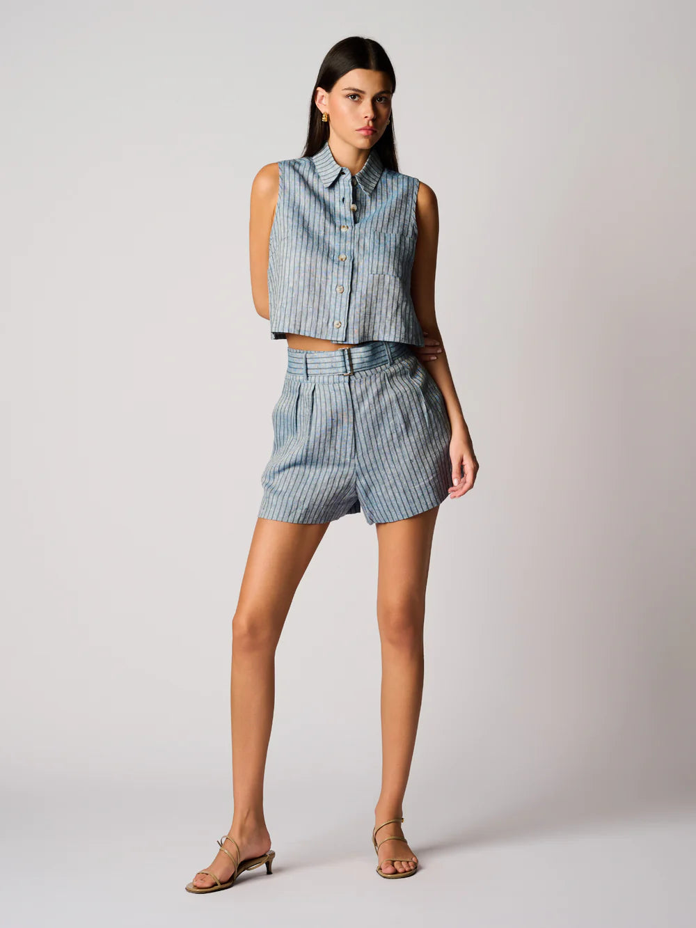 Woman wearing a blue striped sleeveless top and shorts on a light gray background