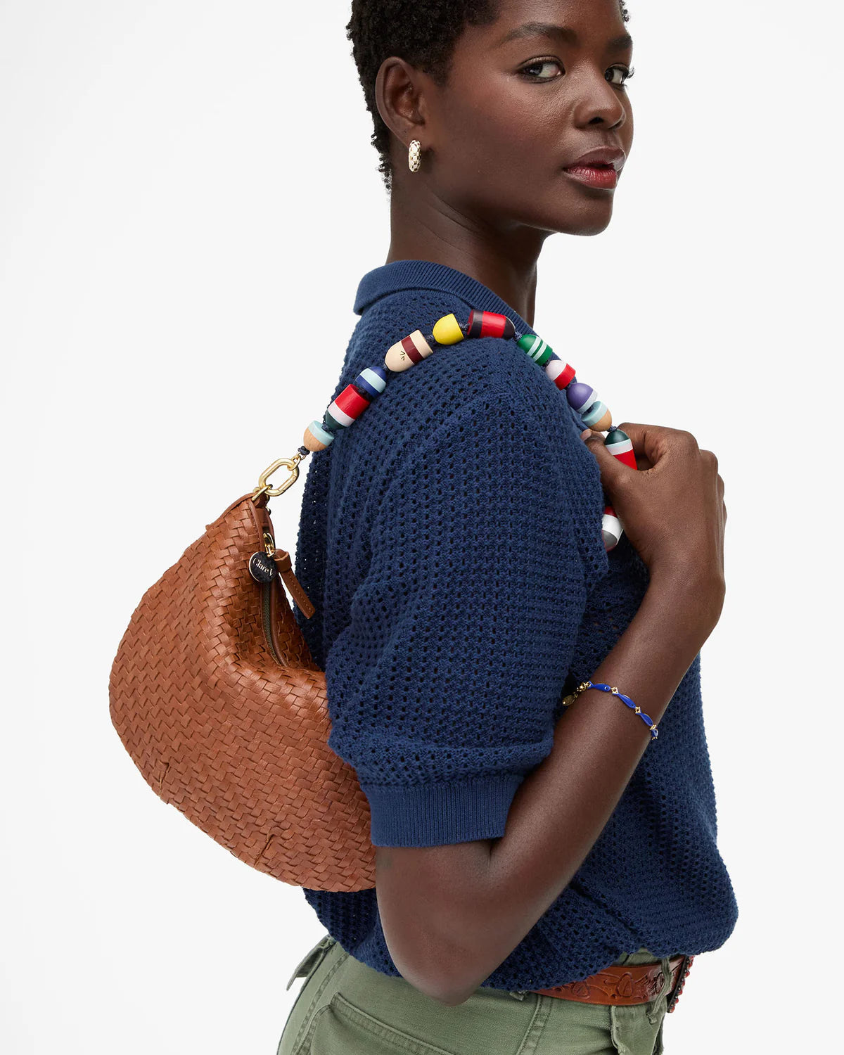 Woman wearing a blue knitted sweater with a colorful beaded accessory, holding a brown woven handbag.