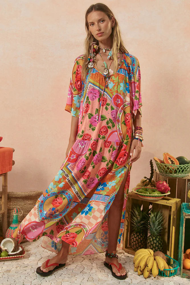 Woman wearing a colorful floral dress standing in a decorative setting with fruits and plants.