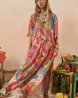 Woman wearing a colorful floral dress standing in a decorative setting with fruits and plants.