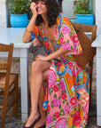 Woman sitting outdoors wearing a colorful floral dress.